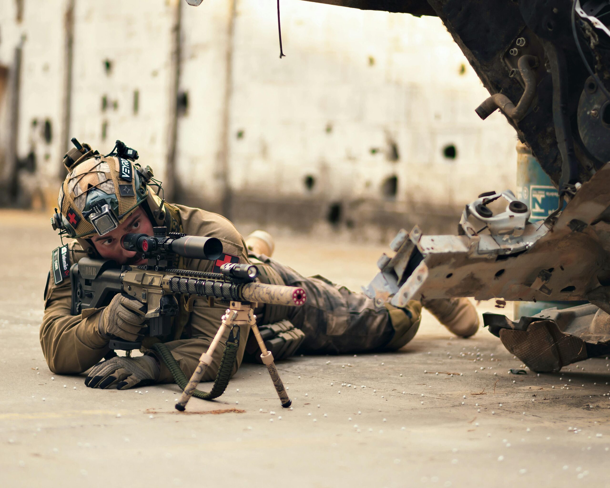 A soldier in tactical gear lying prone with a rifle in an urban setting, showcasing military readiness.
